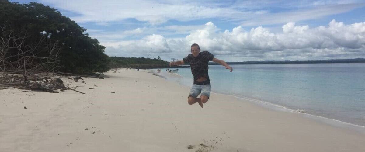 A person jumping on a sandy beach with a calm sea and a cloudy sky in the background.