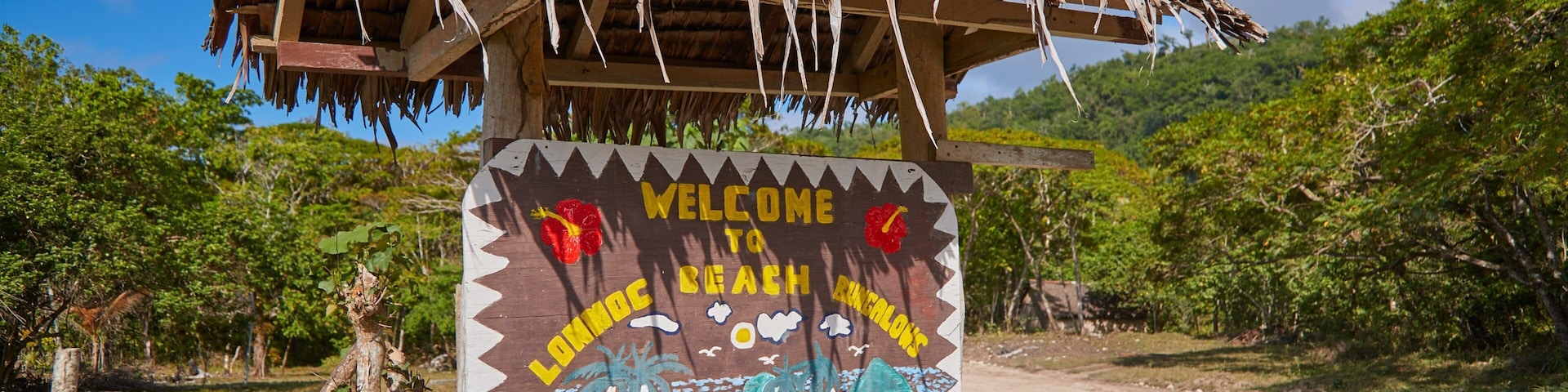 Uma placa de madeira com telhado de palha, dando as boas-vindas aos visitantes aos Bungalows Loma Beach, com restaurante e bar.