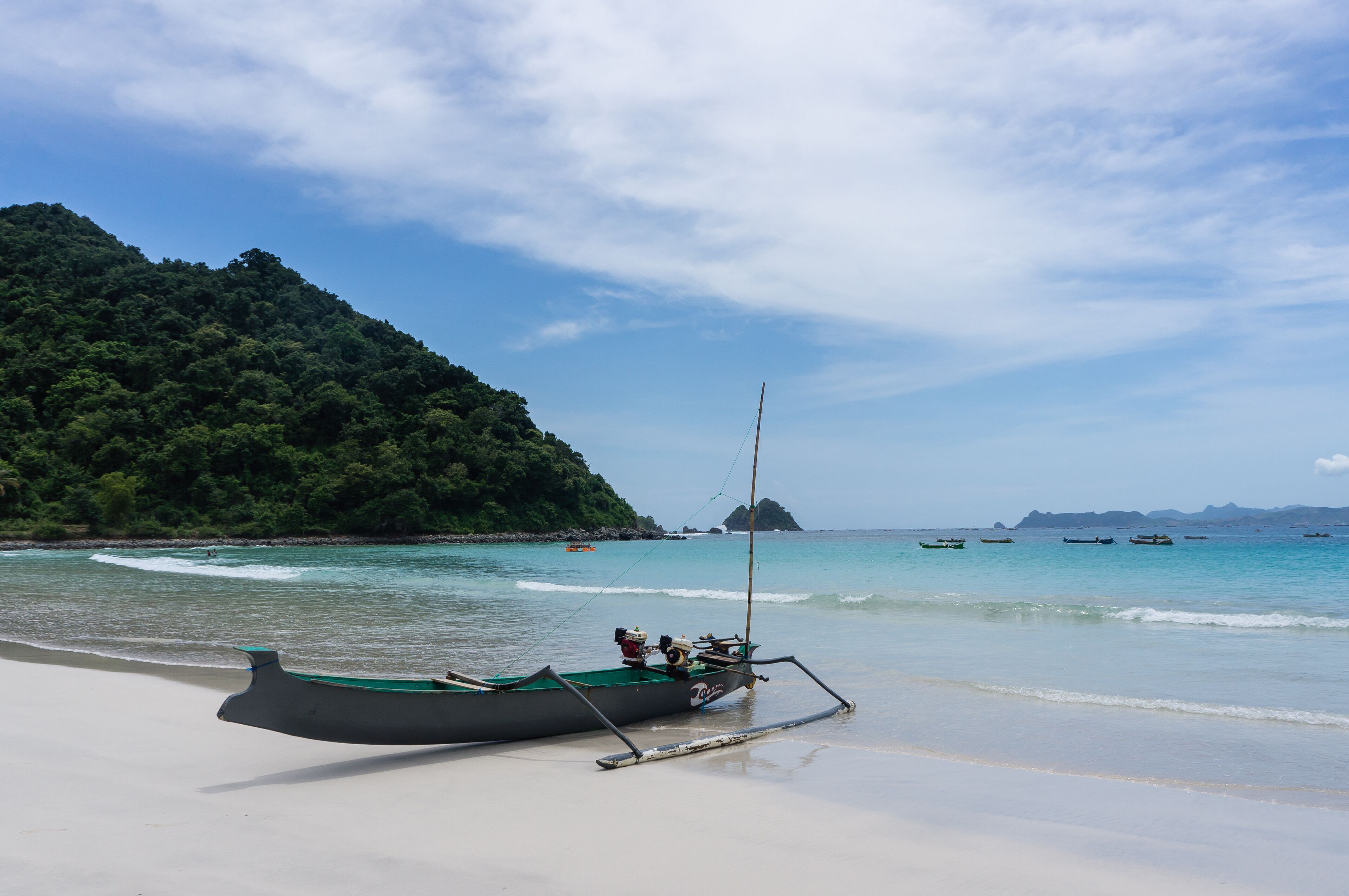 A boat on a beach with clear turquoise water and a forested hill in the background.