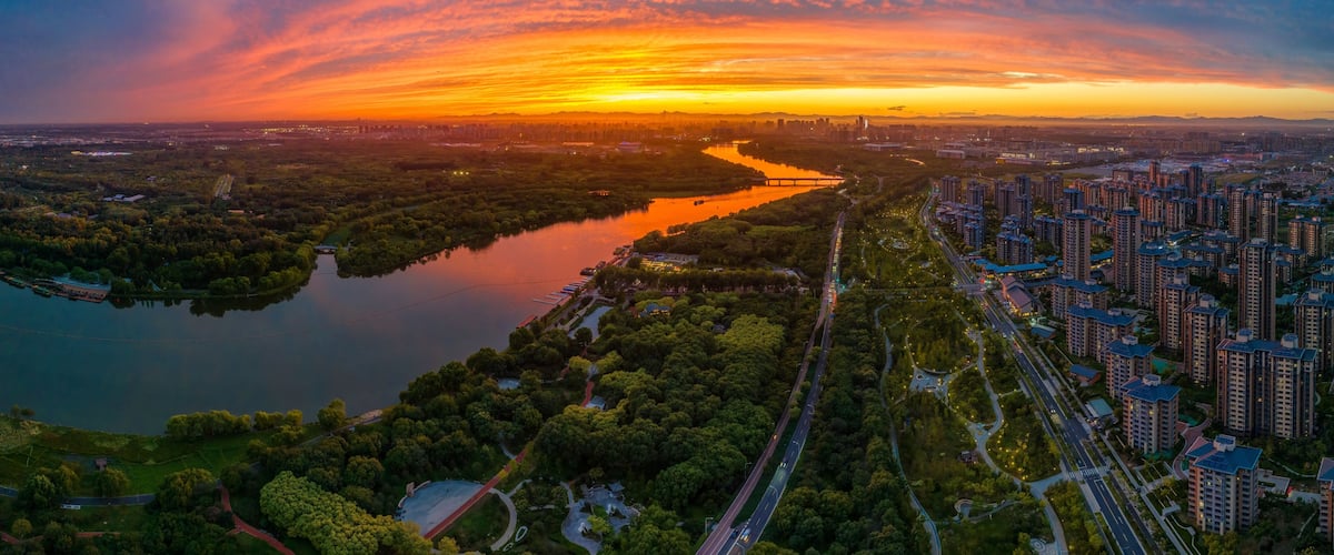 Ein Sonnenuntergang über einem Fluss mit Stadtansicht und Grünflächen.
