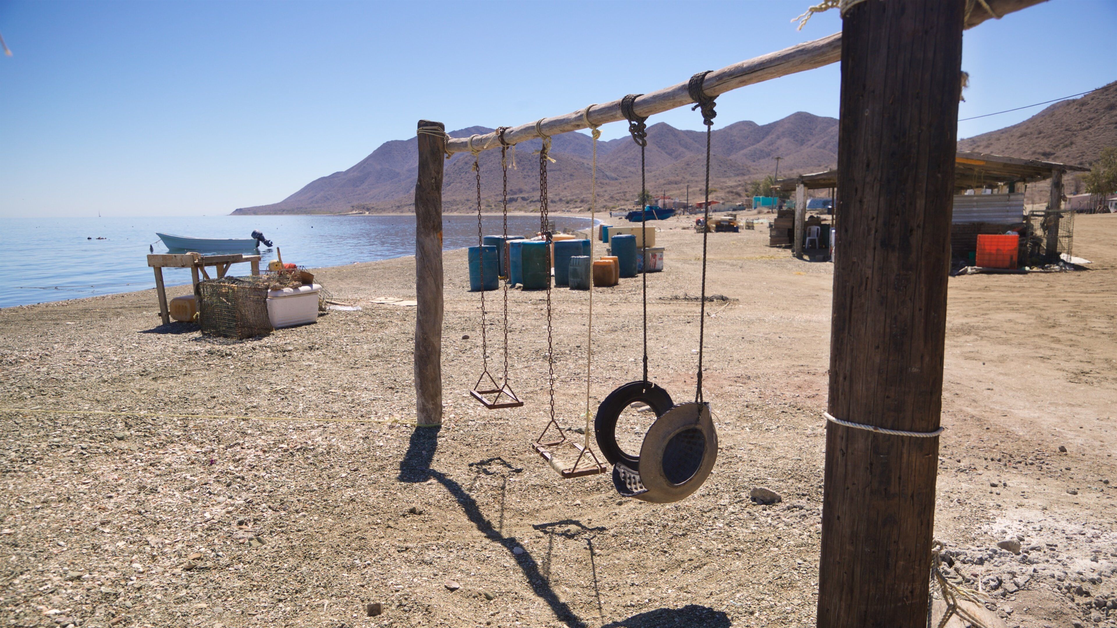 A beach with a swing set, a boat, and storage containers in the background.