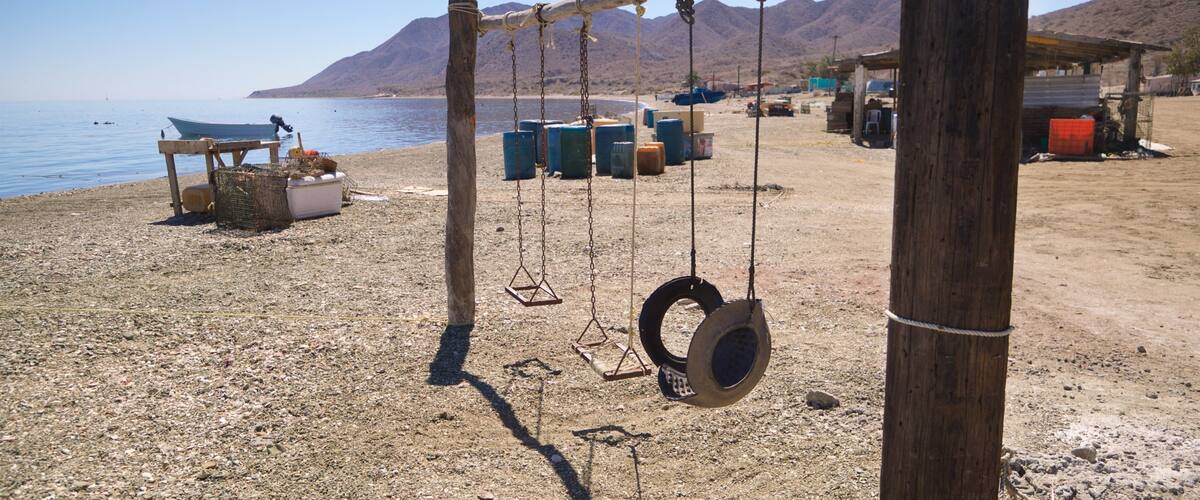 A beach with a swing set, a boat, and storage containers in the background.
