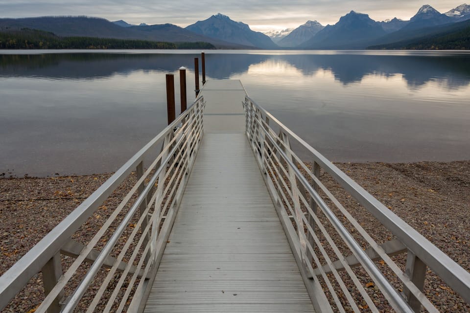 Un molo di legno si protende in un lago calmo, con montagne sullo sfondo.