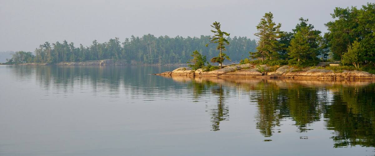 A calm lake with a rocky shoreline and dense forest in the background.
