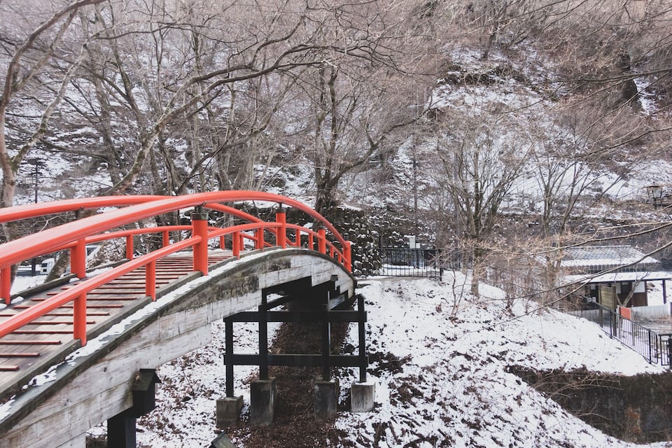 A wooden bridge with red railings in a snowy landscape.