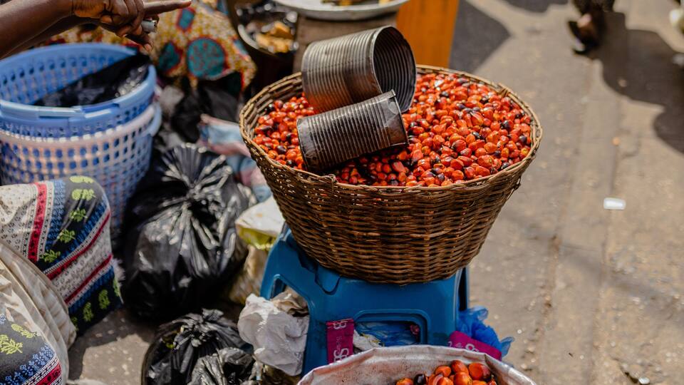 A bustling market with various goods displayed, including baskets of red berries and bananas.