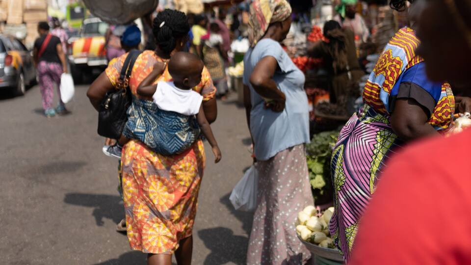 A busy market street with people walking and carrying goods.