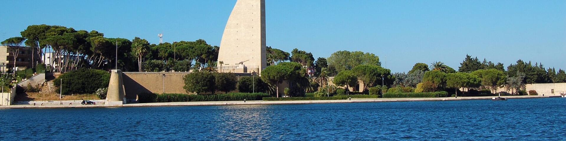 A coastal cityscape with a prominent concrete tower, a clear blue sky, and a calm sea.