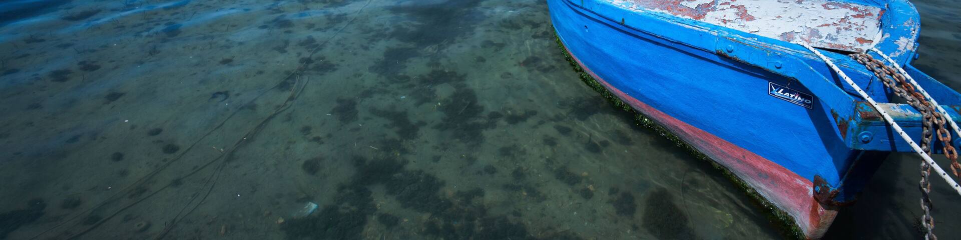 Wooden painted blue fishing boat moored in Porto Cesareo harbour, with rest of harbour in background, sunny spring morning, Sale
