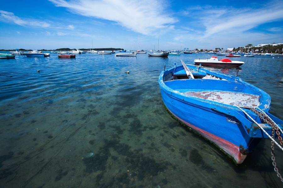 Wooden painted blue fishing boat moored in Porto Cesareo harbour, with rest of harbour in background, sunny spring morning, Sale