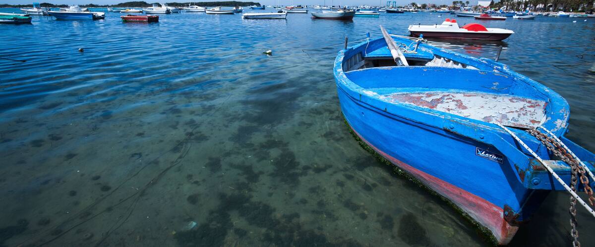 A clear blue boat tied to a dock with other boats in the background.