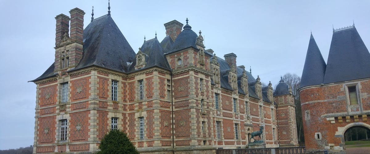 A large, historic building with multiple towers and a prominent statue of a deer.