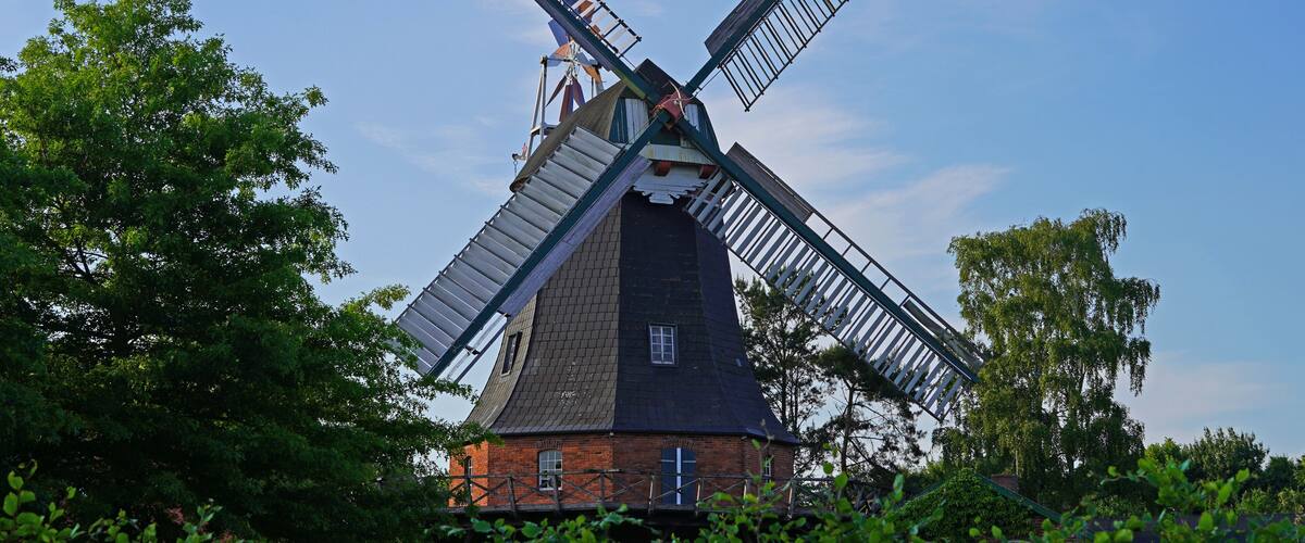 A traditional windmill with a brick base, surrounded by lush green trees.