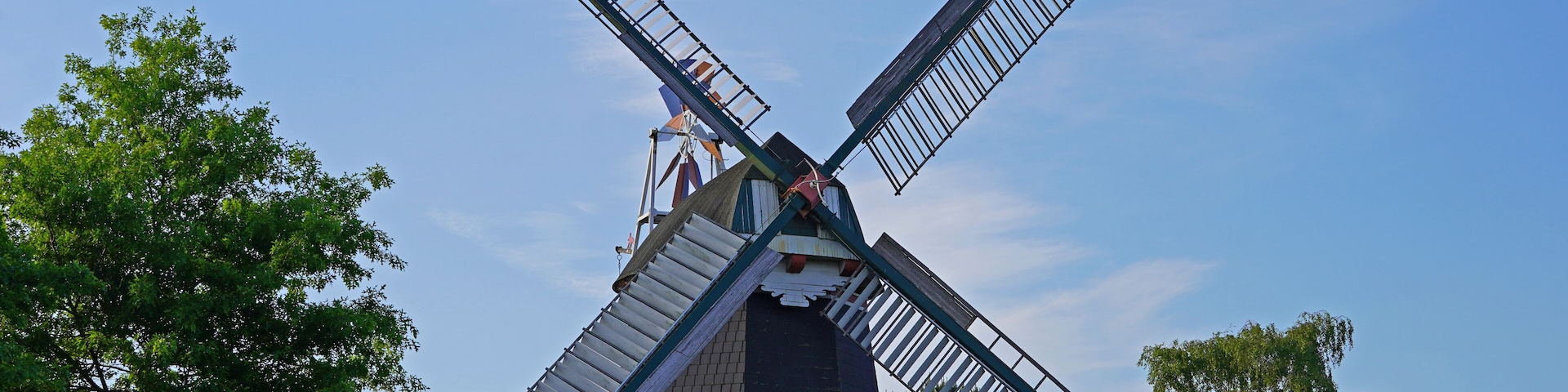 A traditional windmill with a brick base, surrounded by lush green trees.