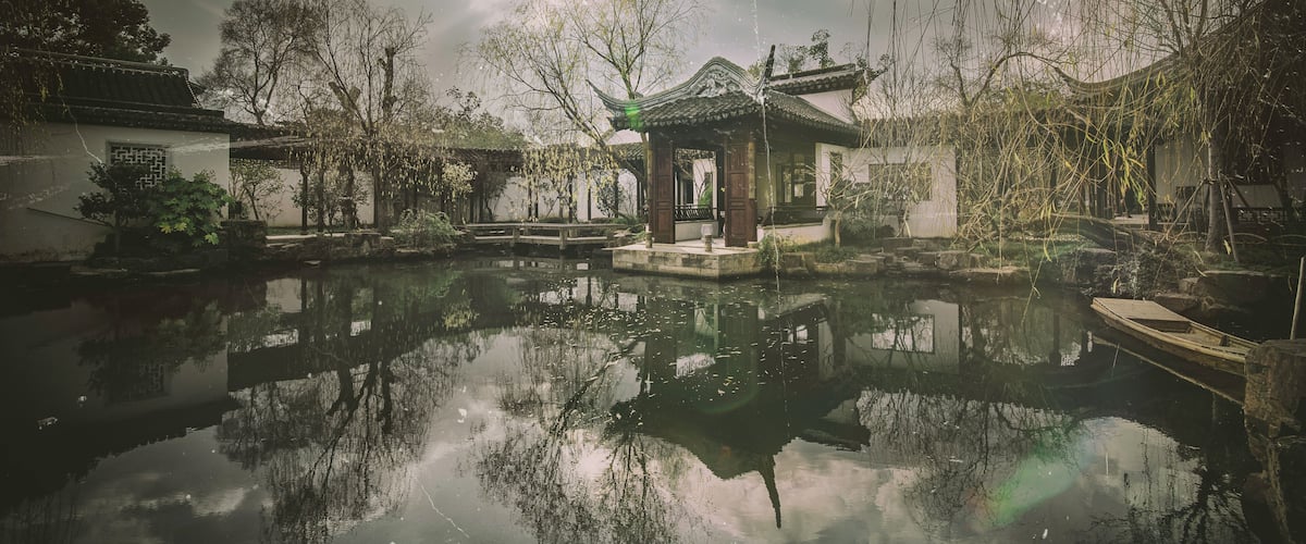 A traditional Chinese courtyard with a pond, reflecting the surrounding architecture and trees.