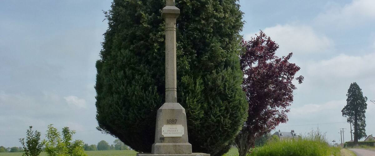 A stone cross monument with inscriptions, surrounded by grass and trees.