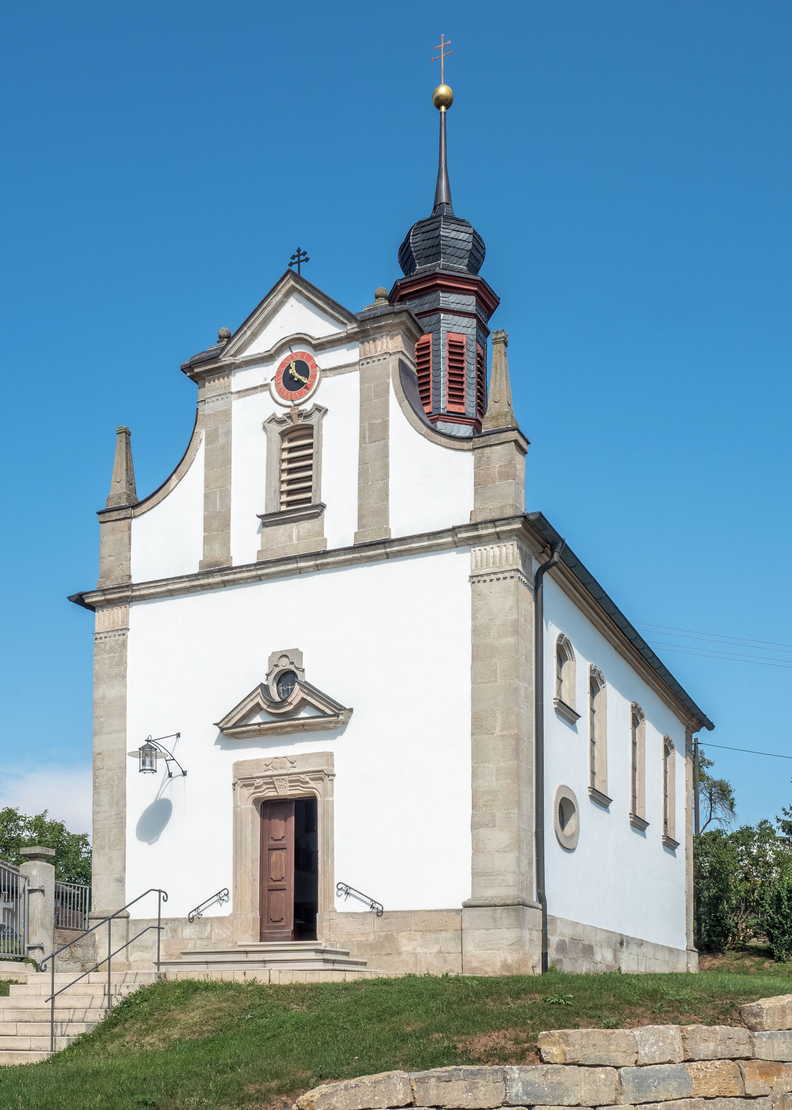 A white church with a clock, a bell tower, and a cross on top.