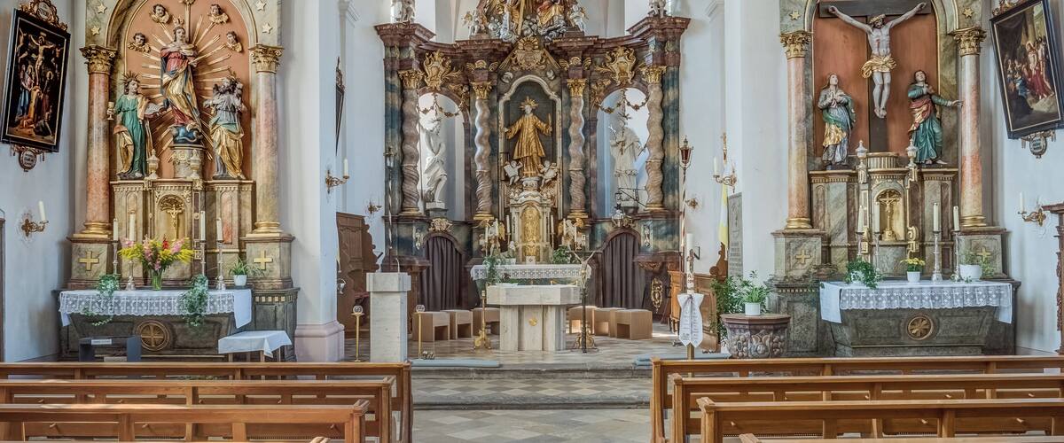 An ornate church interior with a central altar, statues, and wooden pews.