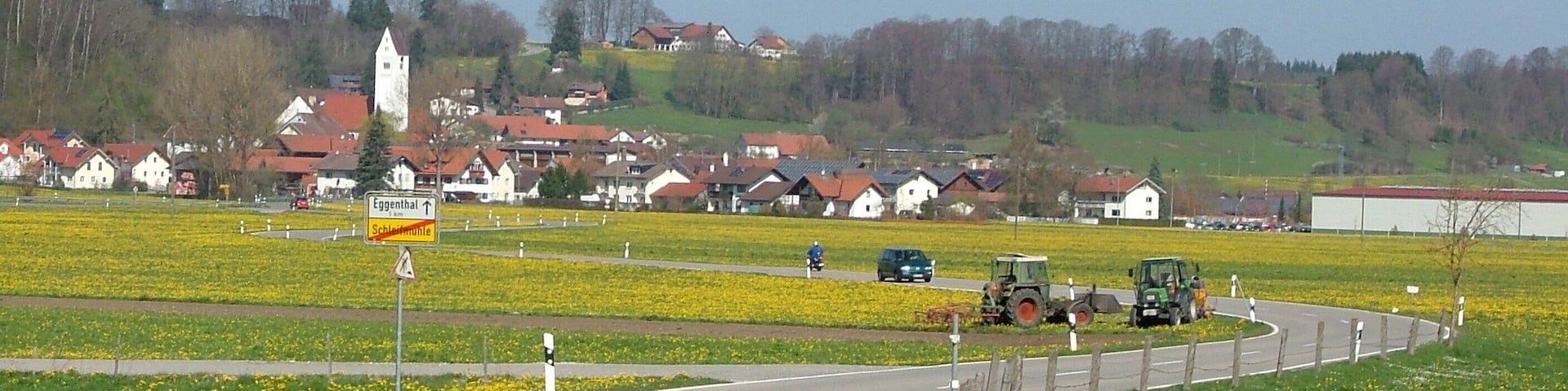 A rural road curving through fields with a village in the background.