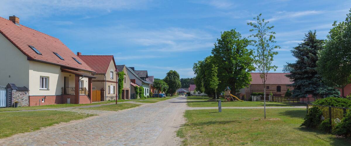 A cobblestone street lined with houses, a playground, and trees.