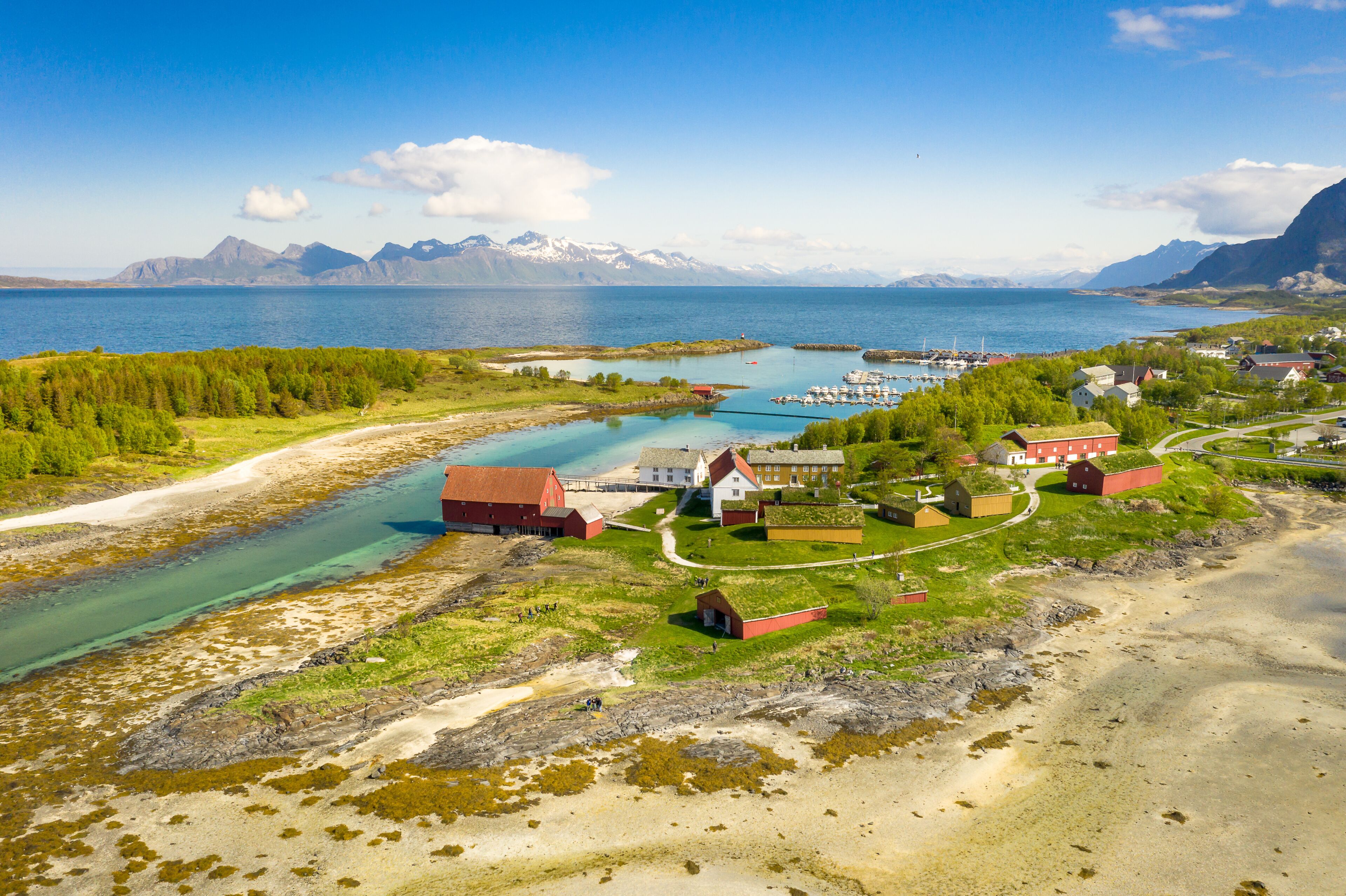A coastal village with a river, boats, and mountains in the background.