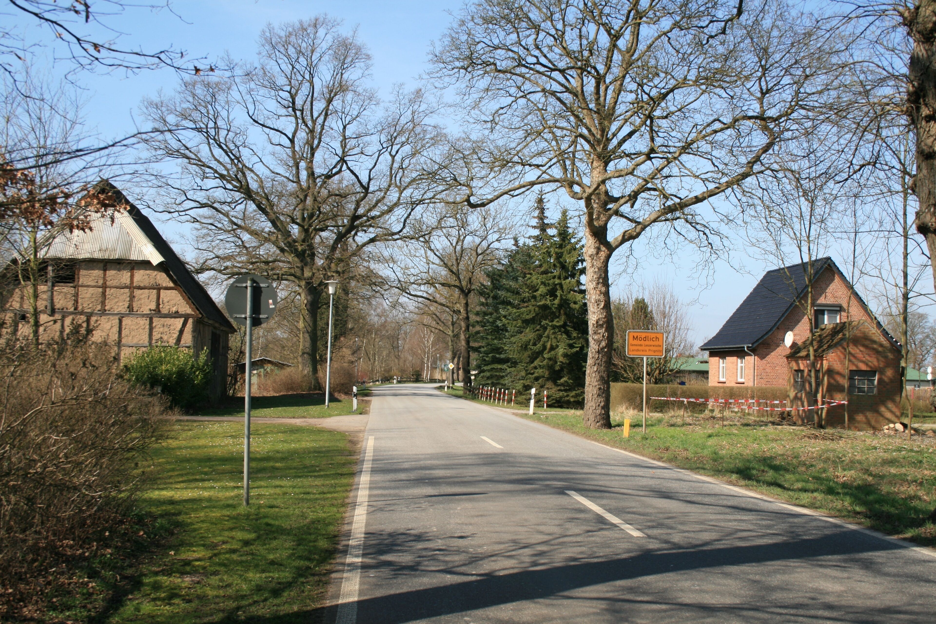 A rural road with a barn on the left, a house on the right, and a sign that reads "Mödlach."