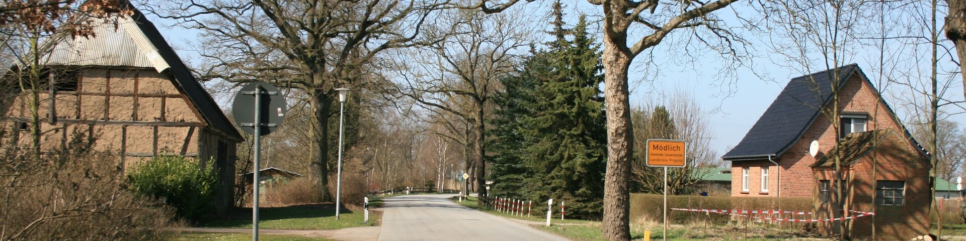 A rural road with a barn on the left, a house on the right, and a sign that reads "Mödlach."