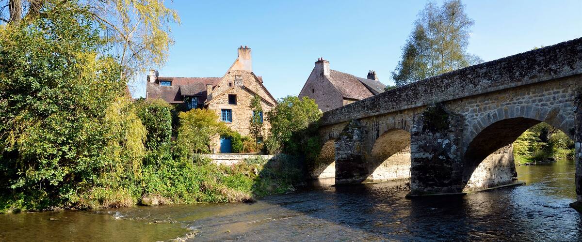A stone bridge over a river with buildings in the background.