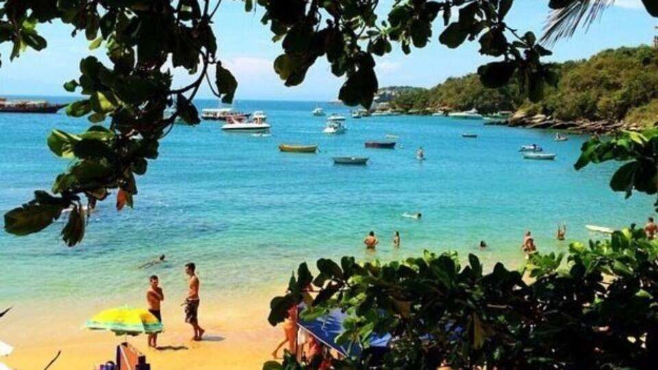 A beach with clear turquoise water, people swimming, and boats in the distance.