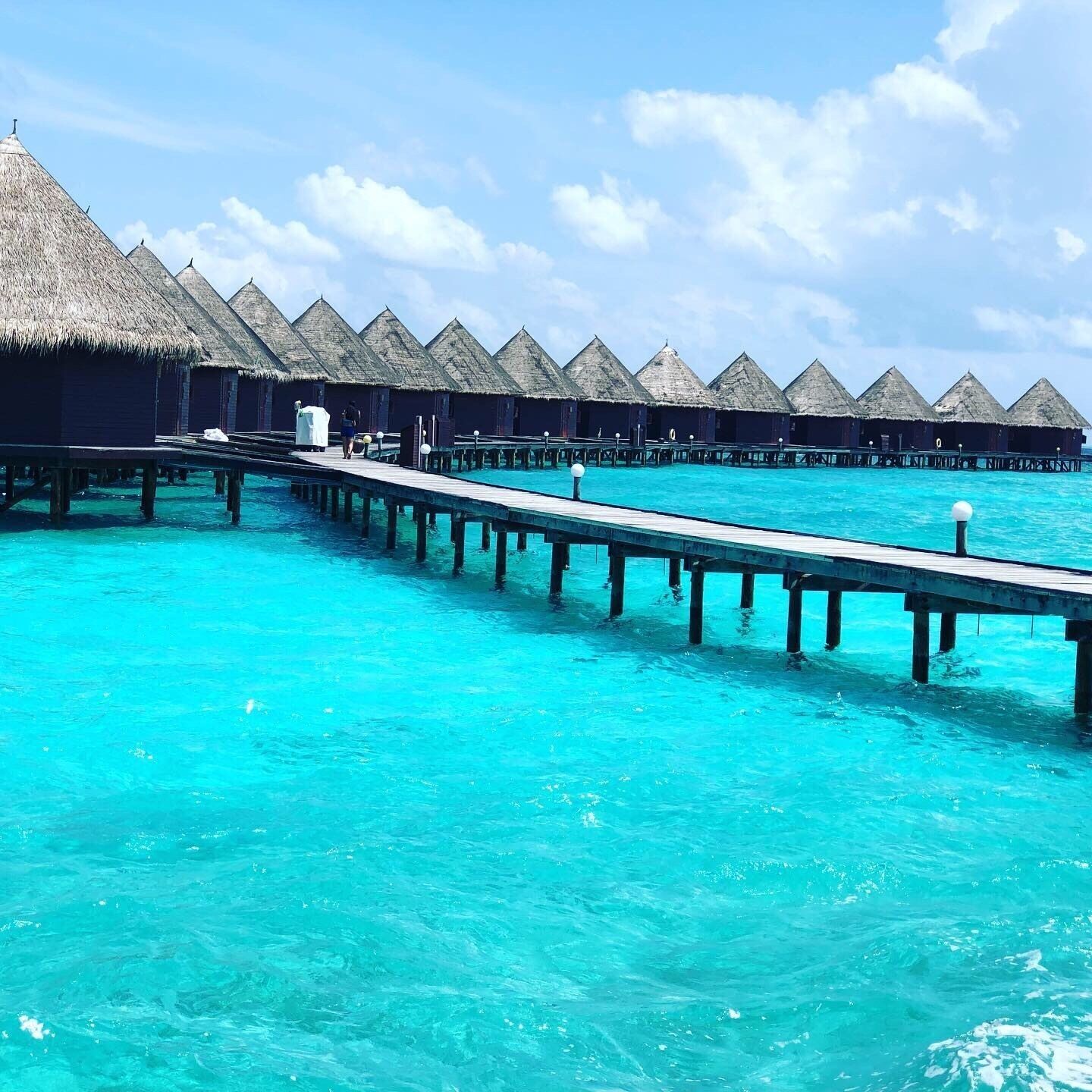 A series of overwater bungalows connected by a wooden pier over turquoise waters.