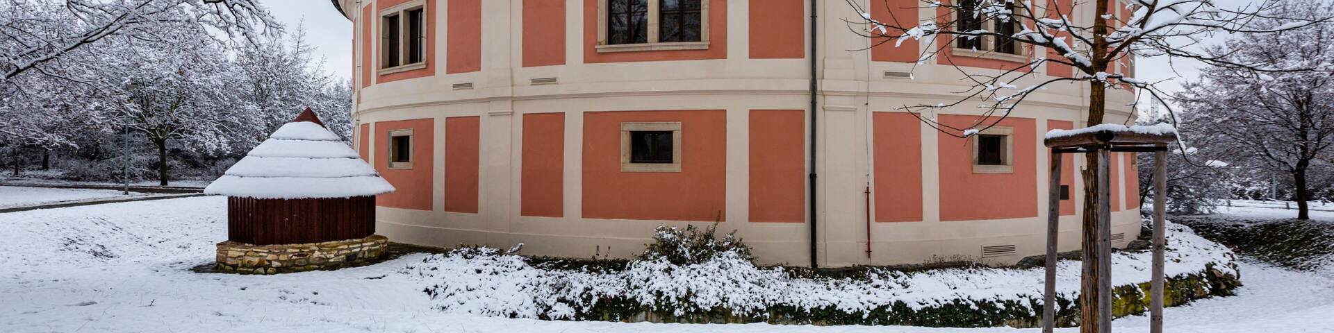 Prague, Czech Republic - January 7 2021: The Chodov fortress with red and pink facade standing in a park. Cloudy winter day with white snow covering ground and trees.
