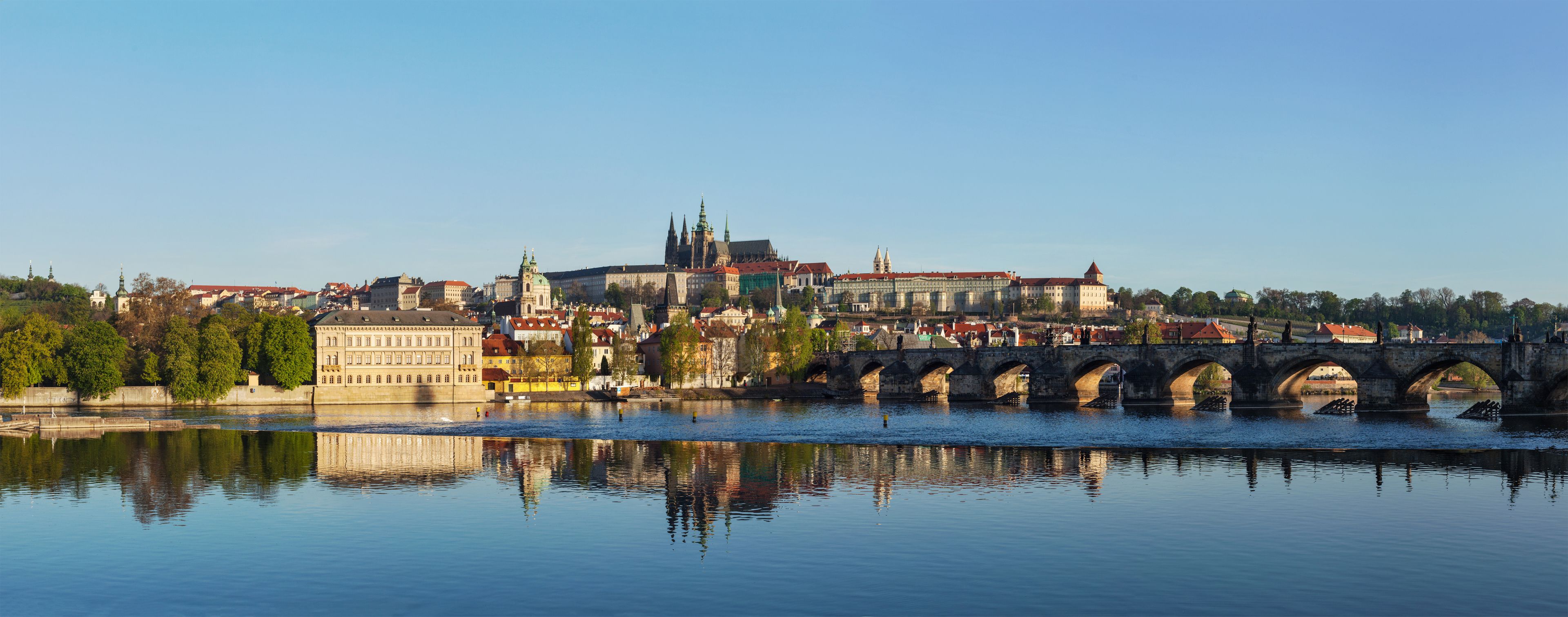 A river with a stone bridge, historic buildings, and a prominent church with a green spire.