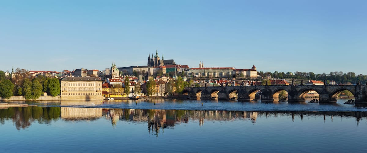 A river with a stone bridge, historic buildings, and a prominent church with a green spire.