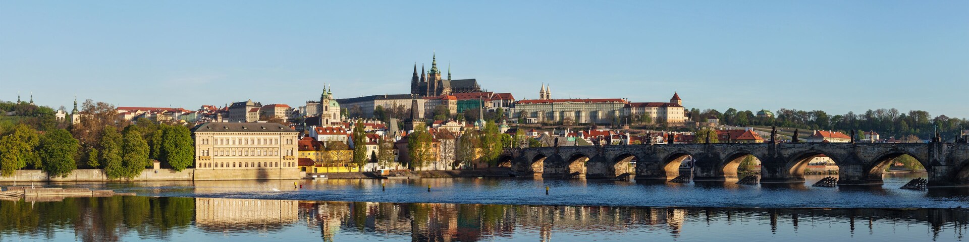A river with a stone bridge, historic buildings, and a prominent church with a green spire.