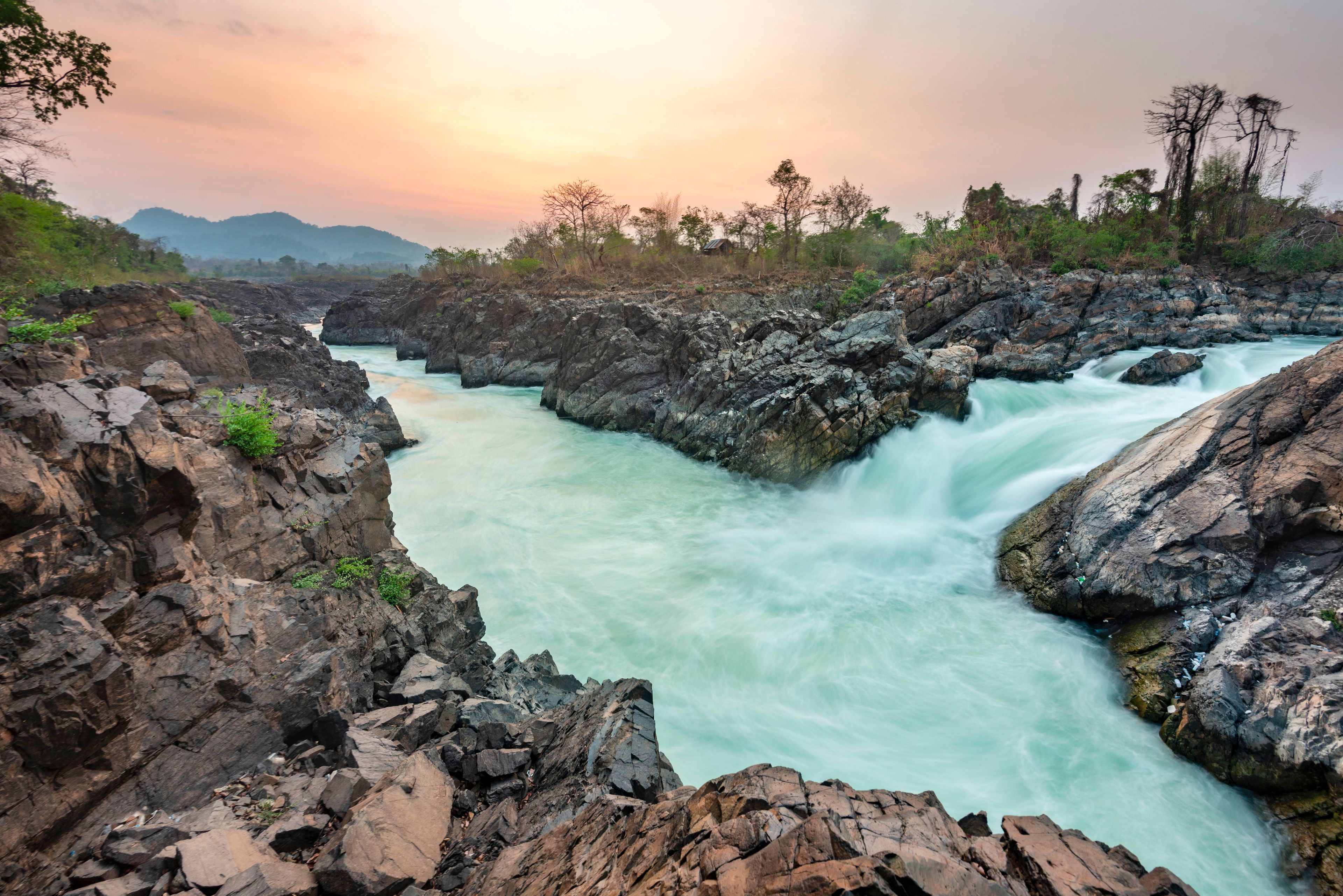 A river flowing through a rocky gorge with a sunset in the background.