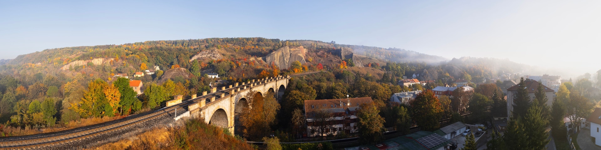 Un puente ferroviario, follaje otoñal y un pueblo enclavado en un valle.