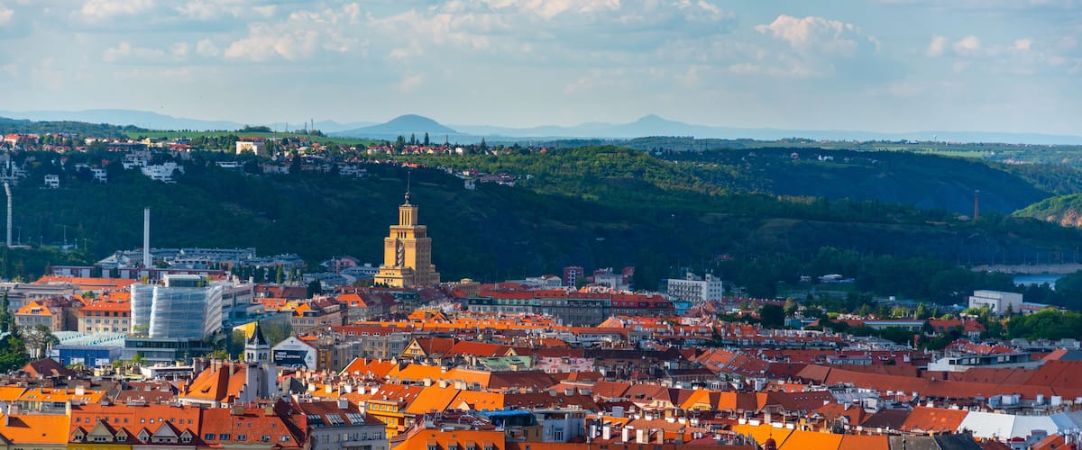 A panoramic view of Prague from a high vantage point, showcasing the iconic Hotel International Tower. Nestled in the distance are the rolling hills and lush greenery that surround the city.
