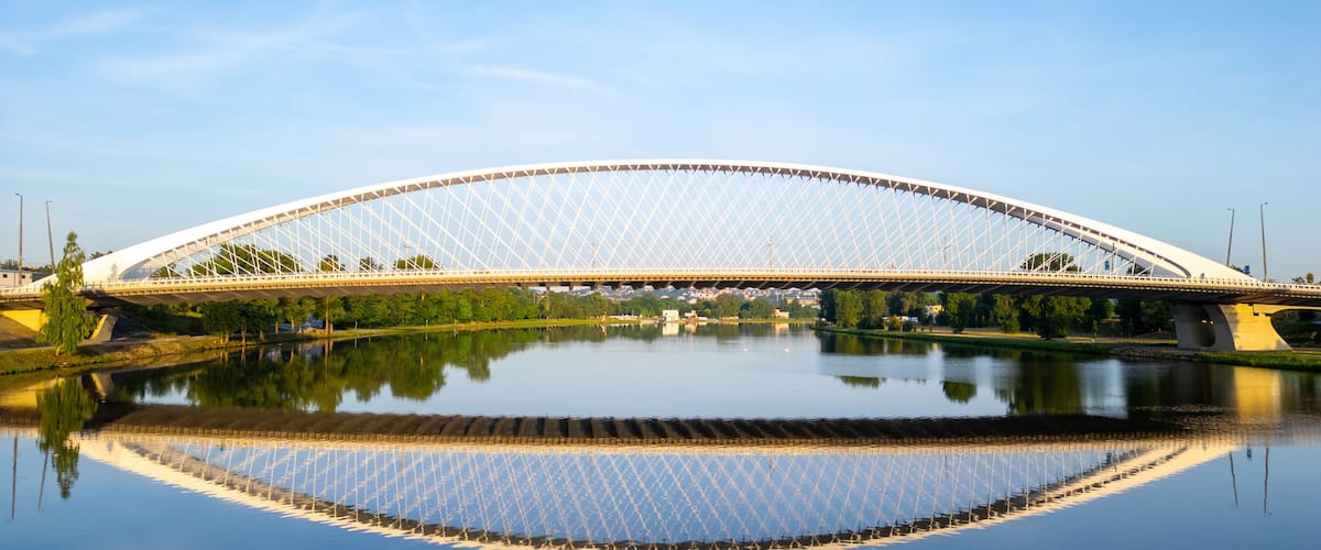 Eine große, weiße Bogenbrücke über einem ruhigen Fluss mit deutlicher Spiegelung.