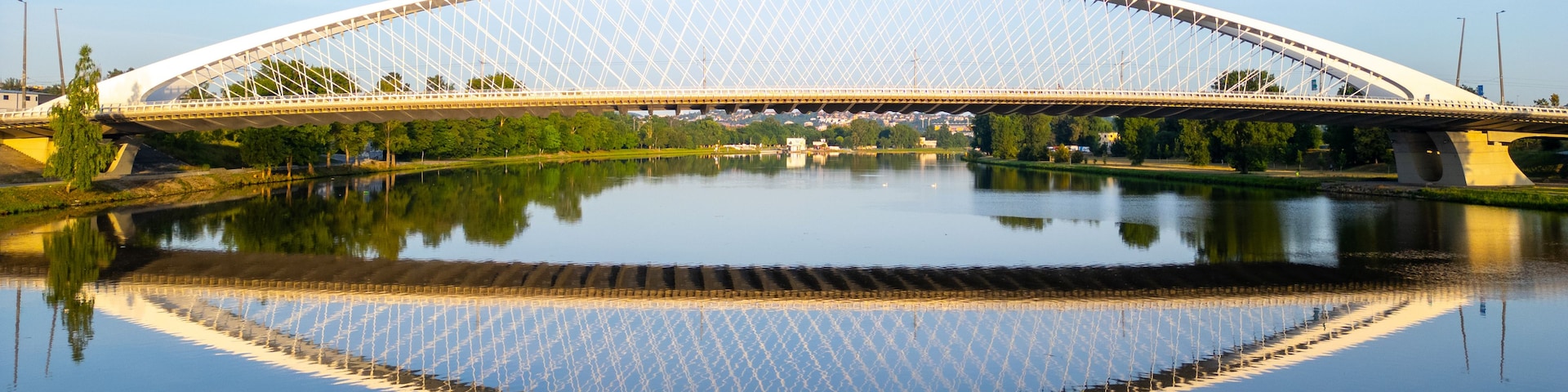 Un puente grande, blanco y arqueado sobre un río tranquilo con un reflejo claro.