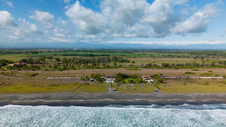 A coastal landscape with a beach, ocean waves, and a distant view of a green valley with scattered houses.