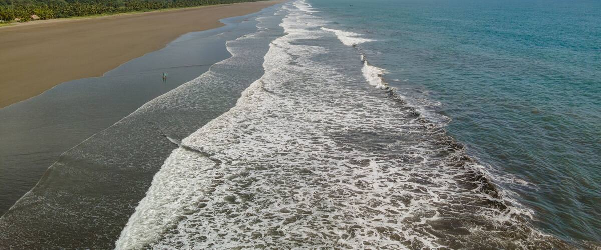 A beach with waves lapping onto the shore, a clear sky, and distant mountains.