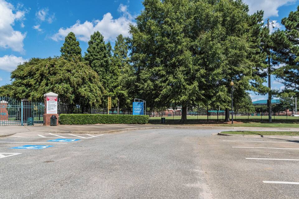 A parking lot with a blue handicapped parking sign, a green fence, and tall trees.