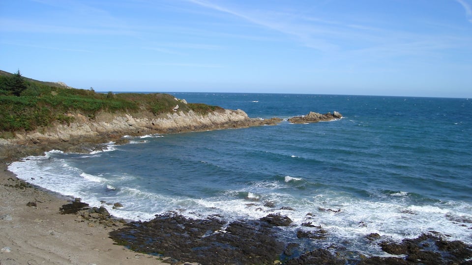 A rocky coastline with waves crashing onto the shore under a clear sky.
