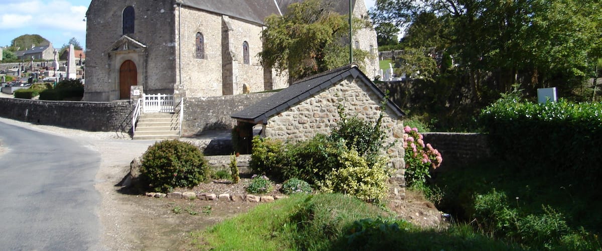 A stone church with a bell tower, surrounded by greenery and a clear sky.