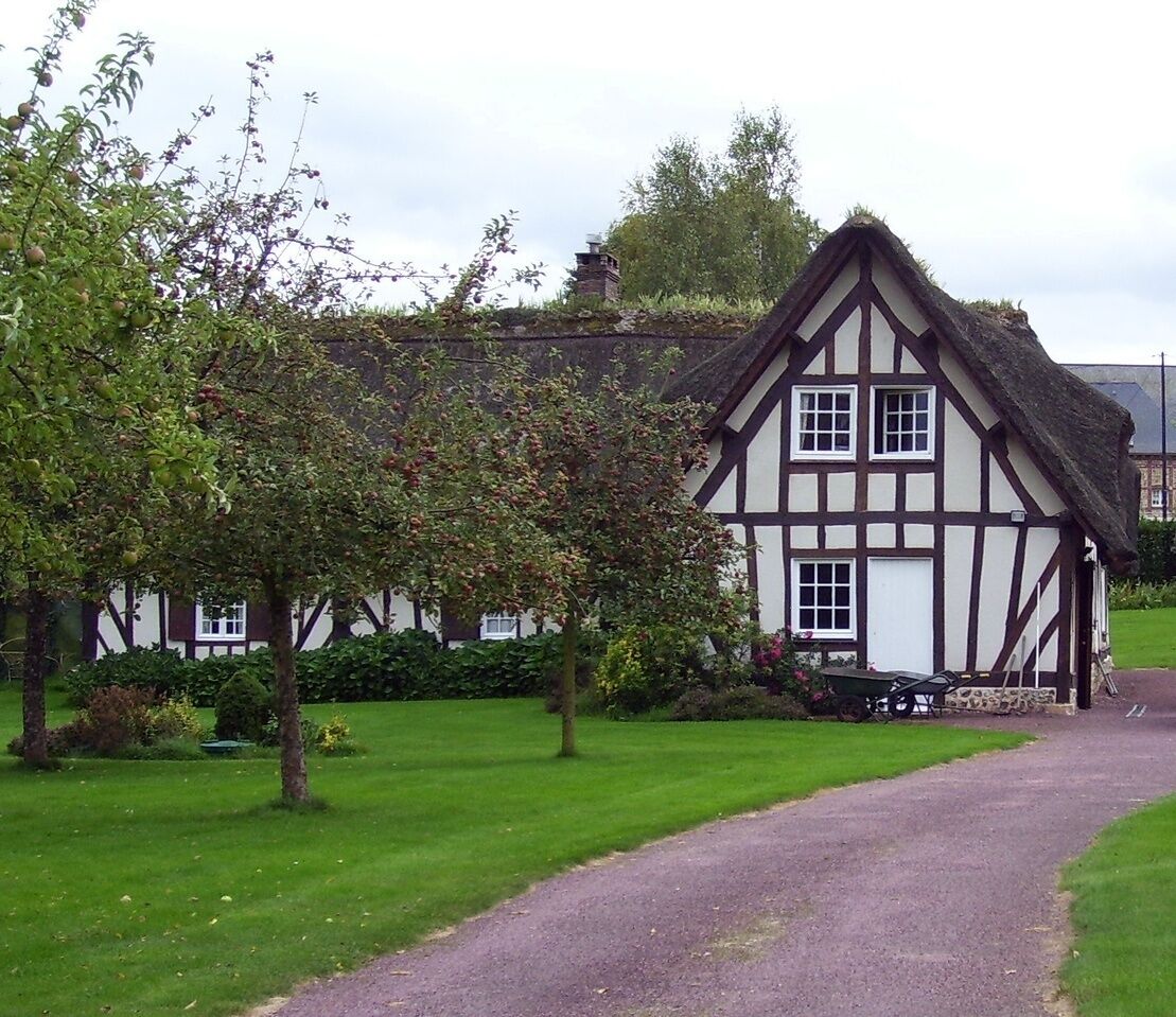 A Tudor-style house with a thatched roof, surrounded by a well-maintained lawn and a gravel path.