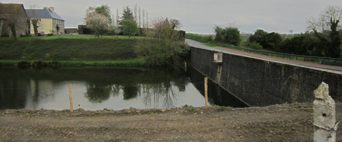 A calm river with a lock, a bridge, and a house in the background.