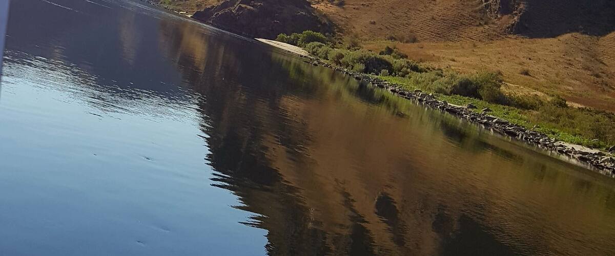 A calm river reflecting the surrounding mountains and clear sky.