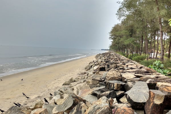 Ein felsiger Wellenbrecher entlang eines Strandes, Wellen schlagen an die Küste.