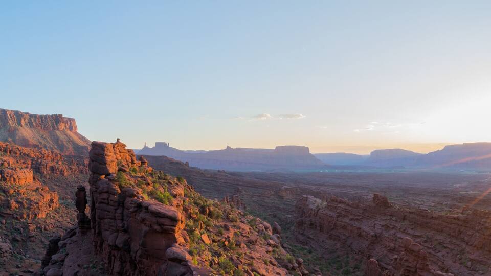 A canyon with a prominent rock formation on the left and the sun setting in the distance.