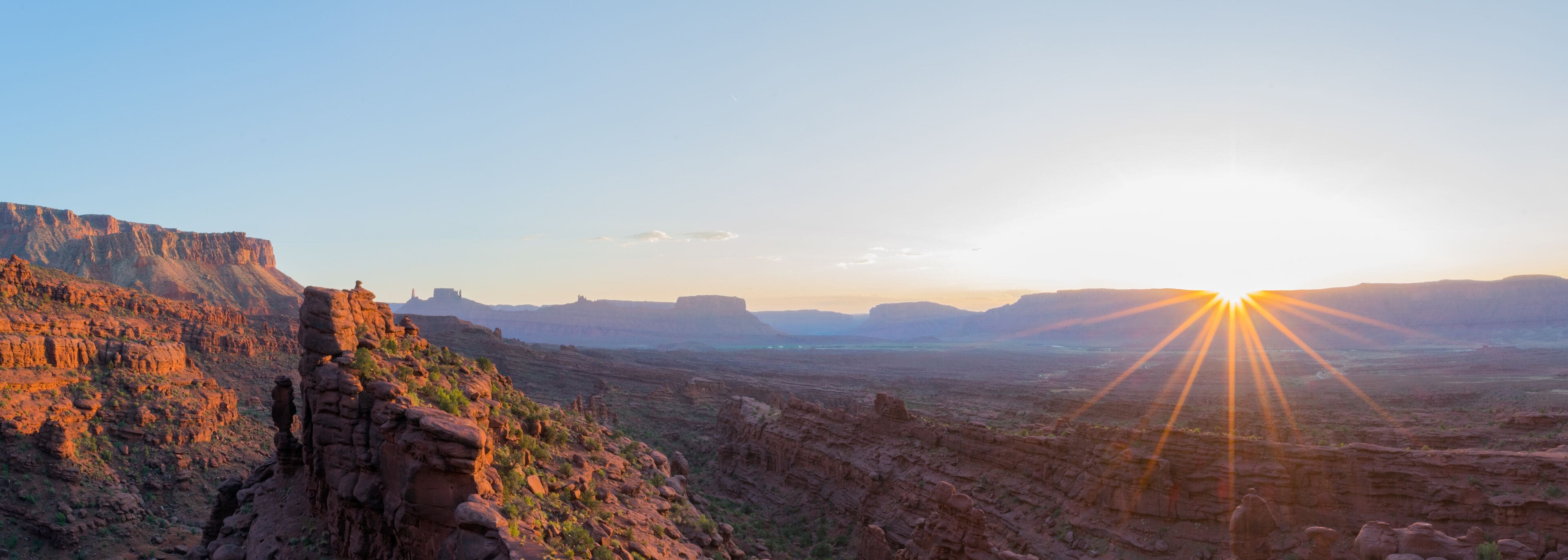 A canyon with a prominent rock formation on the left and the sun setting in the distance.